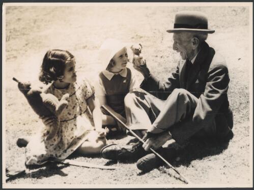 Billy Hughes sitting with two children and holding teddy bear. [picture]