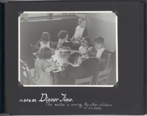 [Photograph of children seated around table being served dinner at] 11.30 a.m., dinner time [picture]