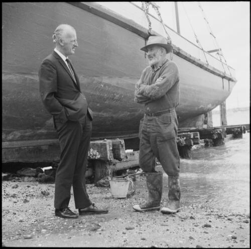 Two men standing next to the hull of a replica of the HMS Endeavour, New Zealand, 1969 / Michael Terry