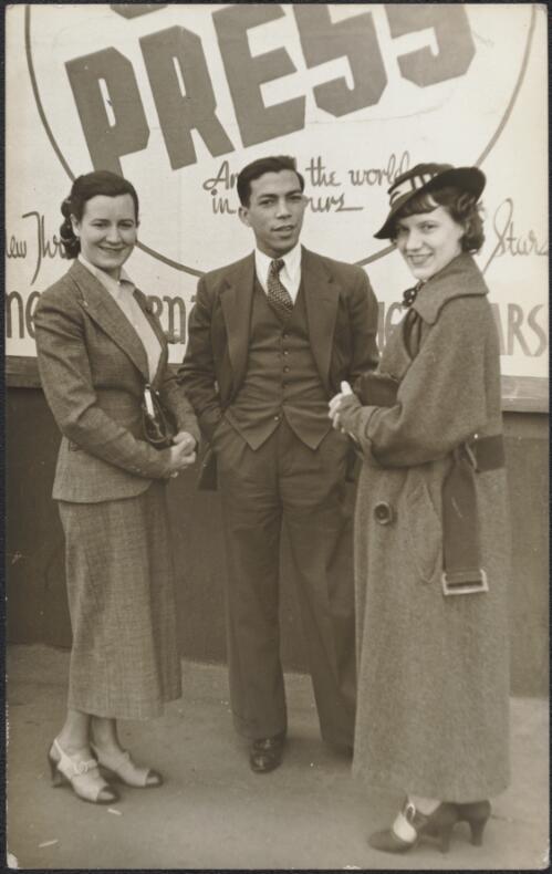 Three performers standing in front of a billboard, 1936