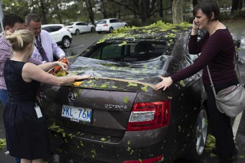 Eleanor Goodwin receiving help from three bystanders to cover her car's rear windscreen with cling wrap after it was damaged in a public car park during a hailstorm, Parkes, Canberra, Australian Capital Territory, 20 January 2020 / Sean Davey