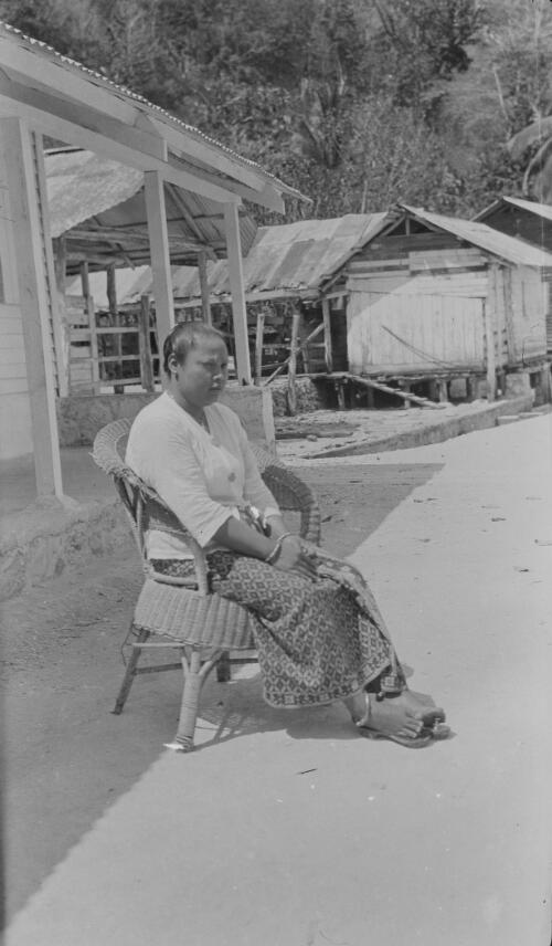 A Christmas Islander woman sitting in a chair in front of a house, Christmas Island, approximately 1920
