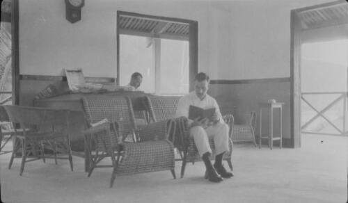 Two men sitting in wicker chairs and reading inside the Christmas Island Phosphate Company building, Christmas Island, approximately 1920