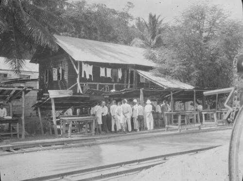 A group of people standing in front of a wooden building next to the railway tracks, Christmas Island, approximately 1927