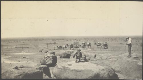 Explorers inspecting weathered granite with camels in the foreground, Cooladding Rockhole, South Australia, 1914 / Alexander Lorimer Kennedy