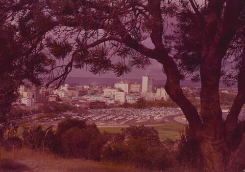 City buildings viewed through the trees from Mount Eliza in Kings Park, Perth, Western Australia, approximately 1958, / Frank Hurley