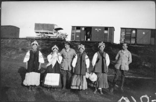 Four women in national costume with two soldiers standing in front of a railway train, Russia, approximately 1918, 1 / Michael Terry