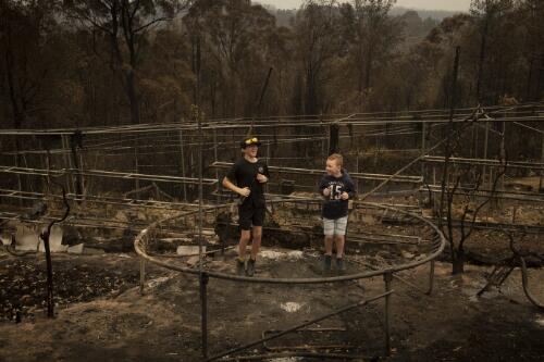 Riley Fletcher and Taz McDermott pretending to bounce on the site of their trampoline destroyed by the Currowan bushfire, Conjola Park, New South Wales, 5 January, 2020 / Matthew Abbott