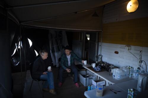Kelvin Pope and Kerry Pope drinking tea near their caravan covered in plastic to protect themselves from asbestos dust from their house destroyed by the bushfires, during the COVID-19 pandemic, Cobargo, New South Wales, 3 May 2020 / Matthew Abbott