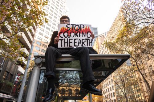 A protester holding a placard sitting on top of the roof of a tram shelter, during the School Strike 4 Climate rally, Melbourne, 21 May 2021 / Leigh Henningham