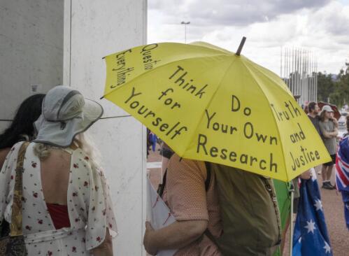 Protester holding an umbrella decorated with protest slogans outside Parliament House, Canberra, 31 January 2022 / Brenton McGeachie