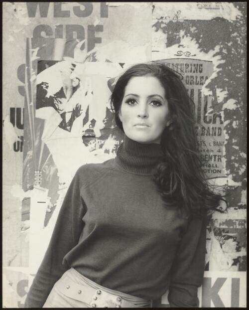 Portrait of a model standing in front of a postered wall / Athol Shmith