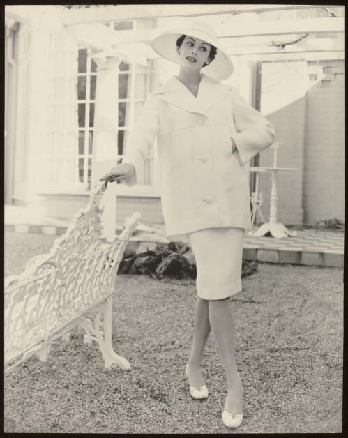 Model wearing a short straight skirt with a jacket, and a hat, approximately 1960 / Athol Shmith