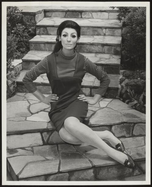 Model wearing striped jumper and pinafore dress sitting on steps, approximately 1965 / Athol Shmith