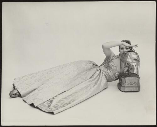 Model wearing ball gown lying beside an ornate bird-cage, approximately 1965 / Athol Shmith