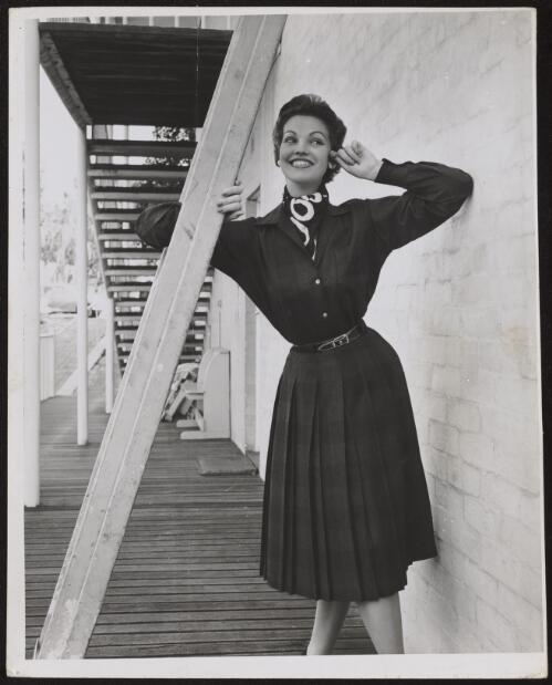 Model wearing a blouse and pleated skirt with a scarf, approximately 1954 / Athol Shmith