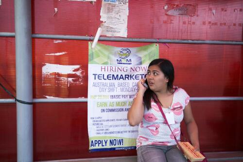 A female employee making a call on her mobile near an advertisement looking to hire telemarkers for the Australian market, Philippines, 28 September 2016 / Dave Tacon