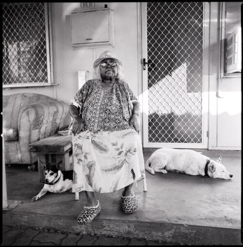 Sheila Sampi sitting on her porch with her two dogs, Port Hedland, Pilbara, Western Australia, 2014