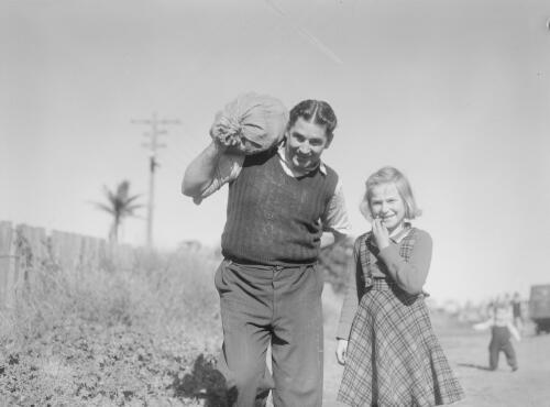 A young girl with a man carrying coal in a potato sack over his shoulder during the coal miner's strike at Newcastle, New South Wales, 1949