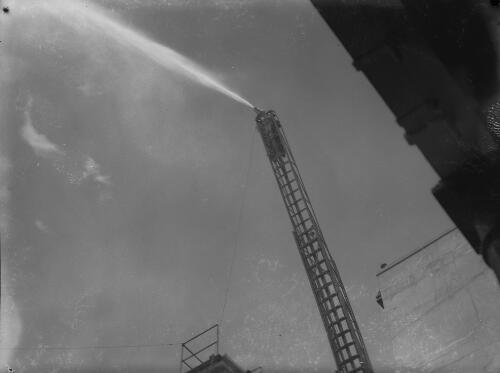 Fireman operating a fire hose at the top of a ladder extended from a fire engine, Newcastle region?, New South Wales, approximately 1950, 1