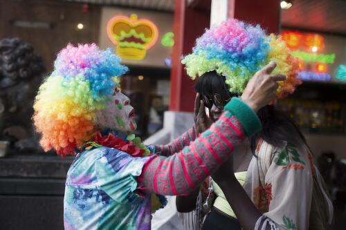 Street performer places a colourful wig on Achingol Mayom's head, Chinatown district, Sydney, 2015 / Conor Ashleigh