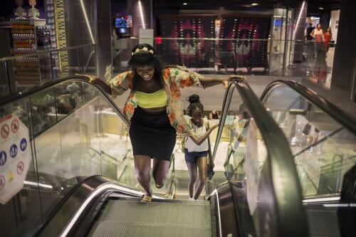 Achingol Mayom and her cousin Agudi on an escalator in a shopping centre, Sydney, 2015 / Conor Ashleigh