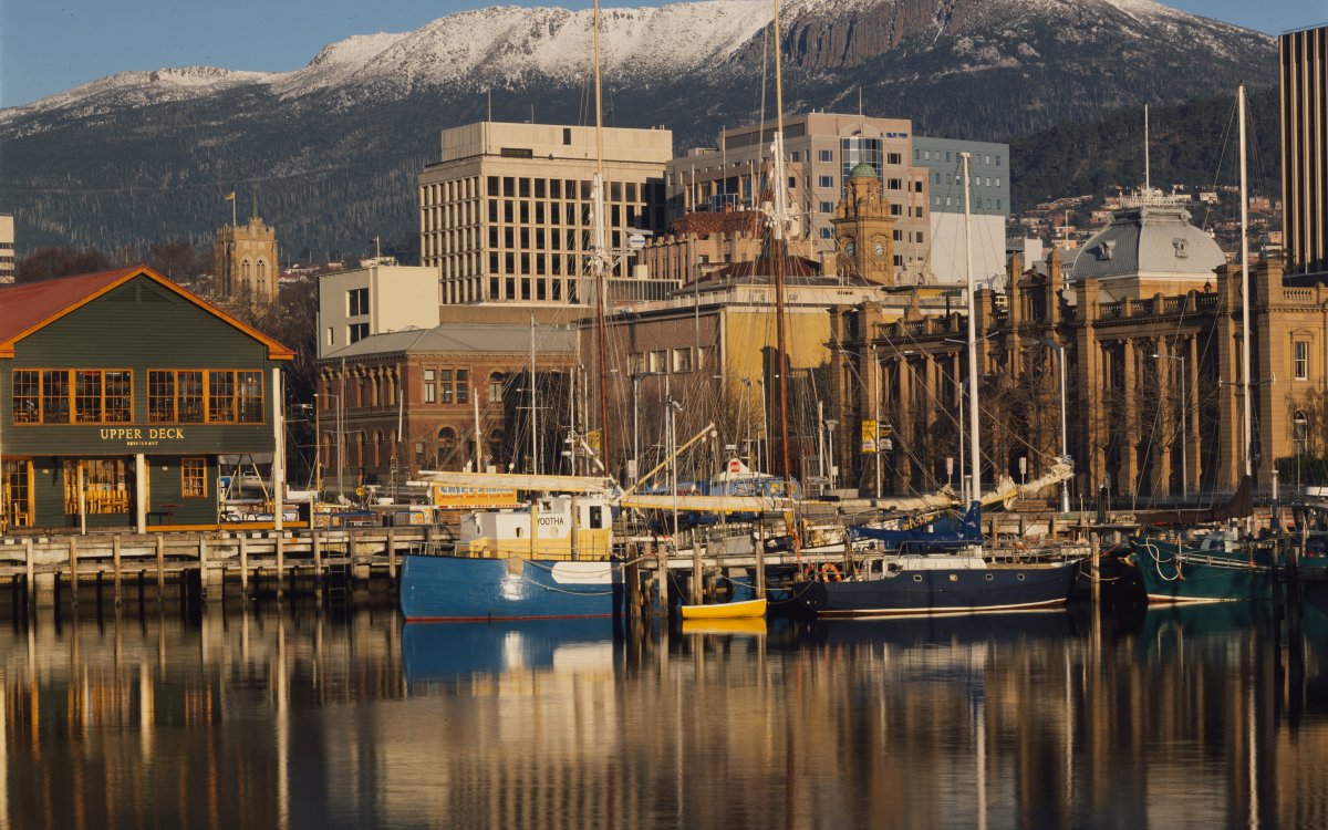 A city harbour scene. In the background a large snow capped mountain. There are several small boats on the water.