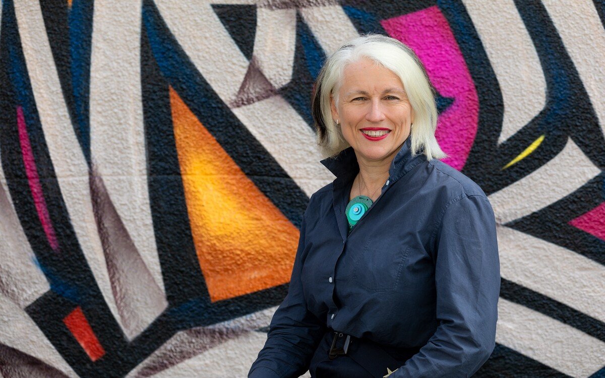 A portrait image of Genevieve Jacobs AM standing in front of a colourful wall