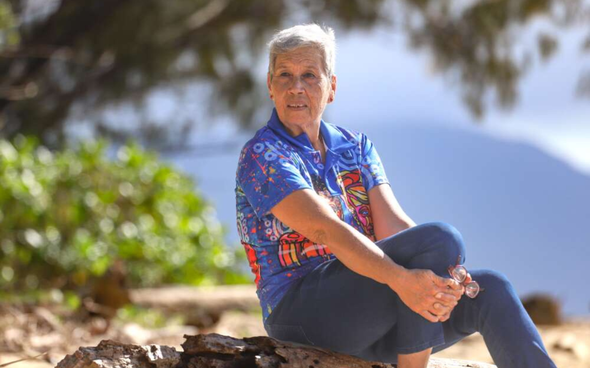 Fijian Australian woman with short grey hair sitting on a rock on a beach