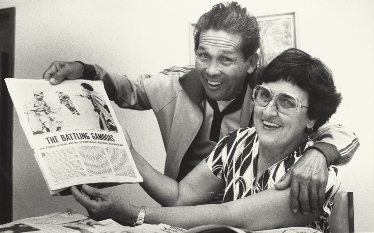 Husband and wife holding up a newspaper article about themselves, with their arms around each other and large smiles