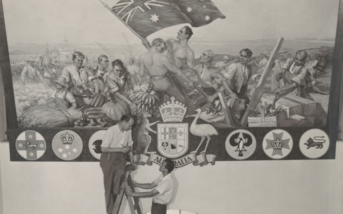 Two men, one standing on a ladder and one holding it steady, looking up at a mural they painted depicting several men holding up an Australian flag