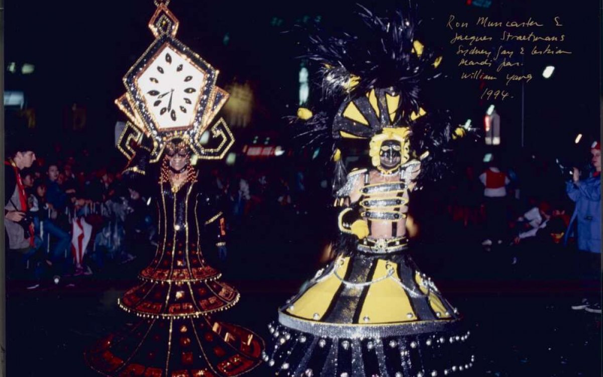 Two people in a night time parade dressed up in large, intricate, colourful costumes.