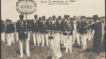 Group of men in white pants and dark blazers standing in a field. One of them holds a previous version of the Australian flag and another a sign that Reads 'Australie'