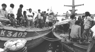 Two boats with rope hanging between them filled with men, women and children coming from Vietnam
