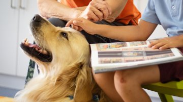 Two people reading a book with a dog sitting between them.