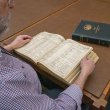 Man reading through a thick, leather-bound book of shipping registers