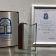 A silver and wooden plaque, glass trophy and framed certificate for the 2024 CBCA Laurie Copping Award given to the National Library