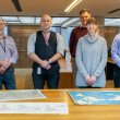 Two women and four men, who make up the Library's family history team, standing and smiling in the Special Collections Reading Room in front of a table with three maps on it