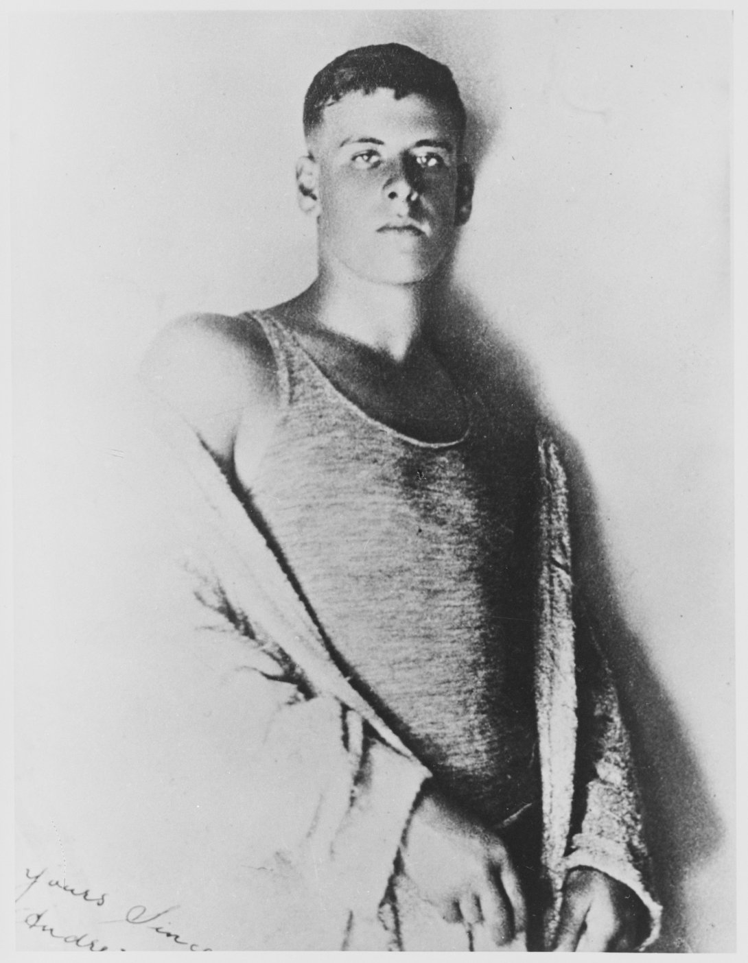 Black and white photo of young male swimmer wearing a singlet and robe looking seriously at the camera