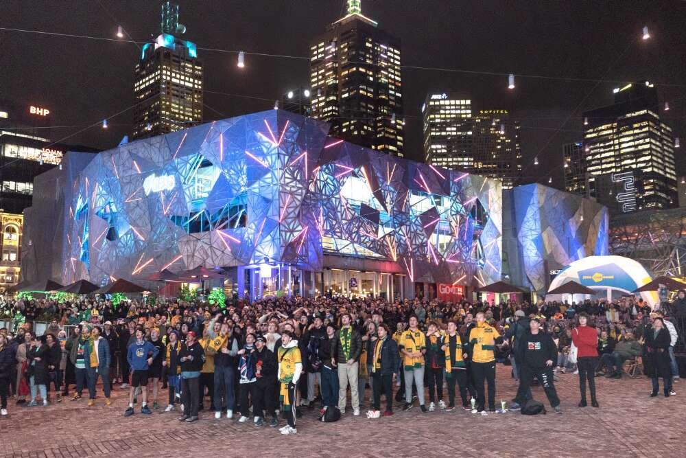 A large crowd of people in a square in front of a lit up cube-shaped building.