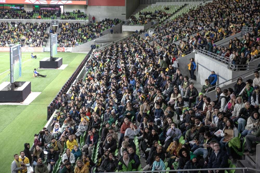 A crowd of people sitting in the stands at a sports stadium.