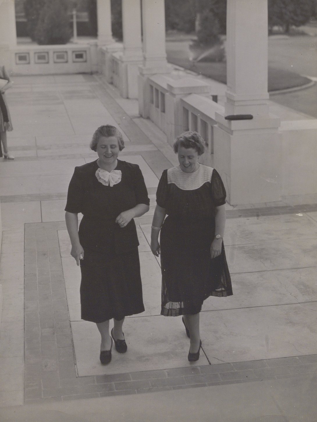 Black and white photo of two women, Dorothy Tangney and Enid Lyons, walking together towards the entrance of Old Parliament House 