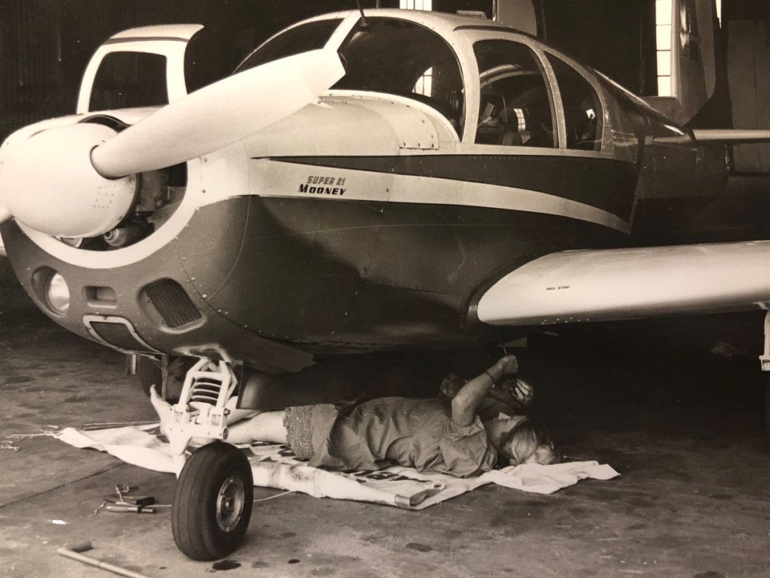 Woman lying down under a plane repairing it