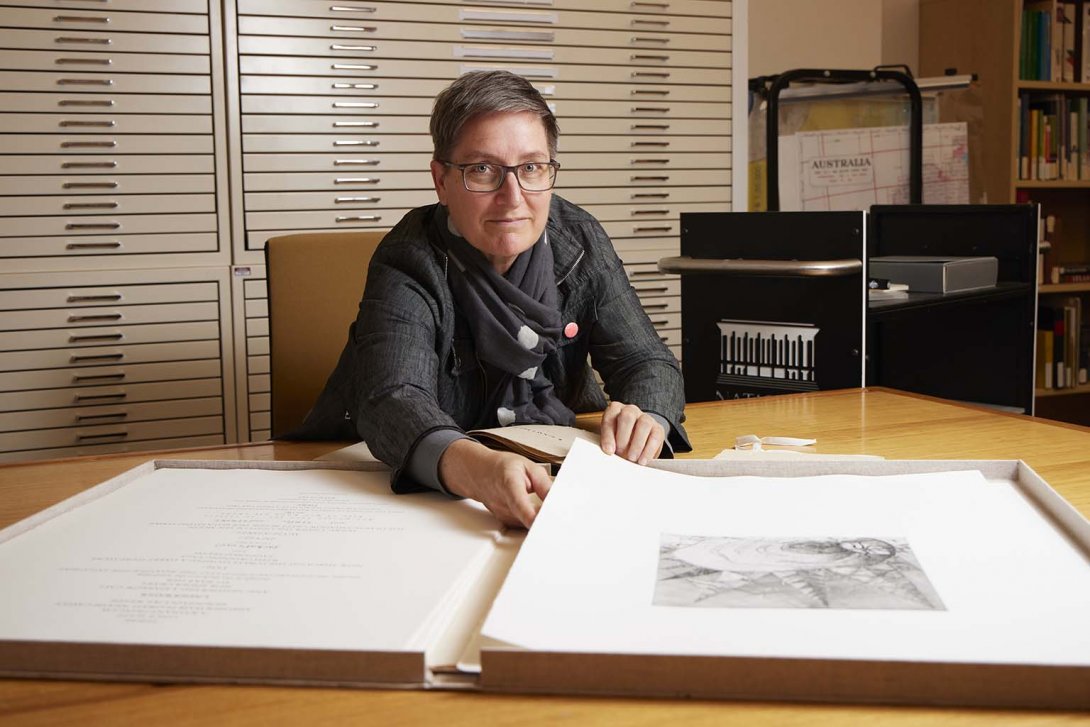 Dr Caren Florance sits at a desk with a large book of images